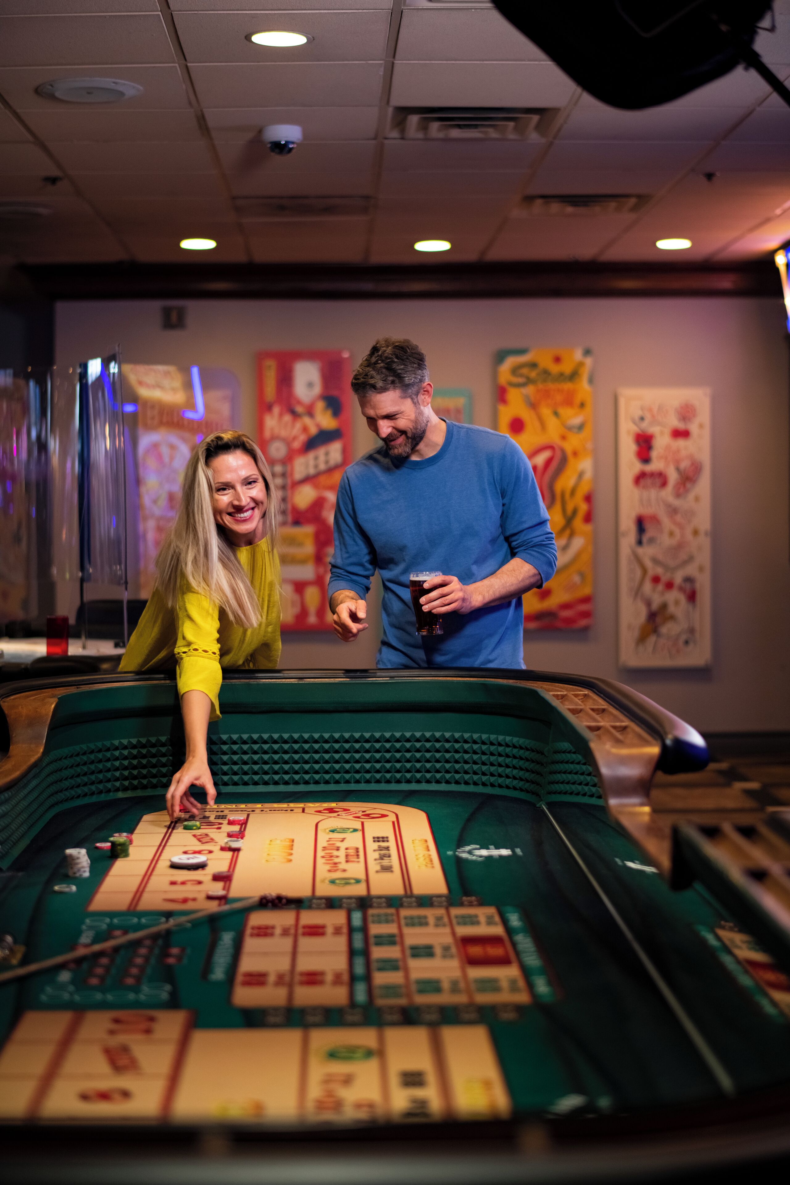 Une table de craps dans un casino, avec une femme penchée au-dessus et un homme debout à côté d'elle.