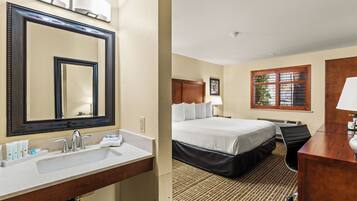 A hotel room with a large mirror, a bed, a desk, and a window with blinds.