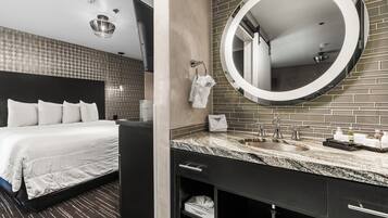 Een moderne hotelkamer met een groot bed, een ronde spiegel, een granieten aanrechtblad en een donkergrijze kledingkast.