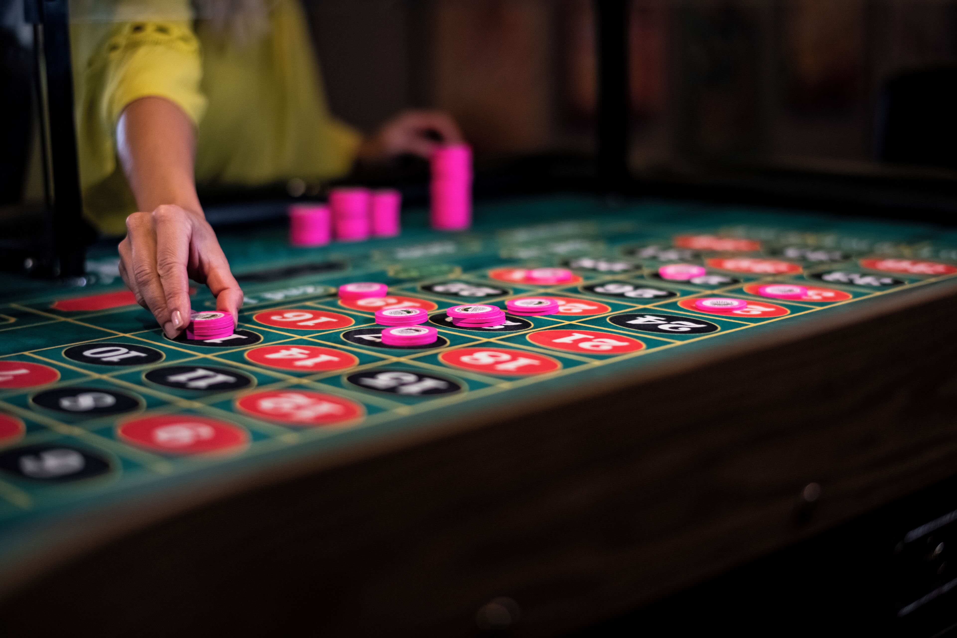 Gros plan sur une table de casino, où une main dépose une jeton rose sur un emplacement.
