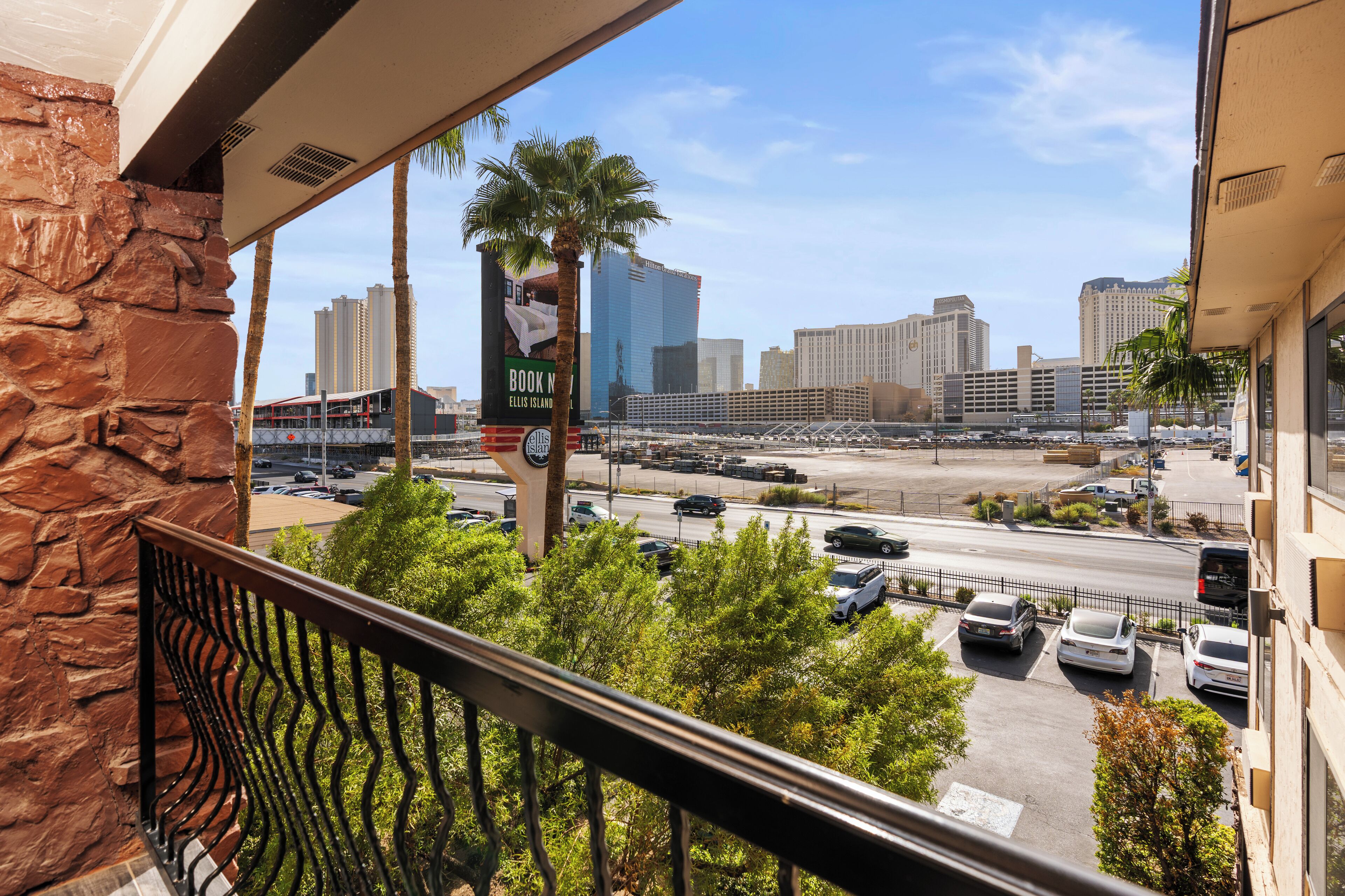 A balcony with a stone wall and metal railing overlooking a parking lot and city skyline.