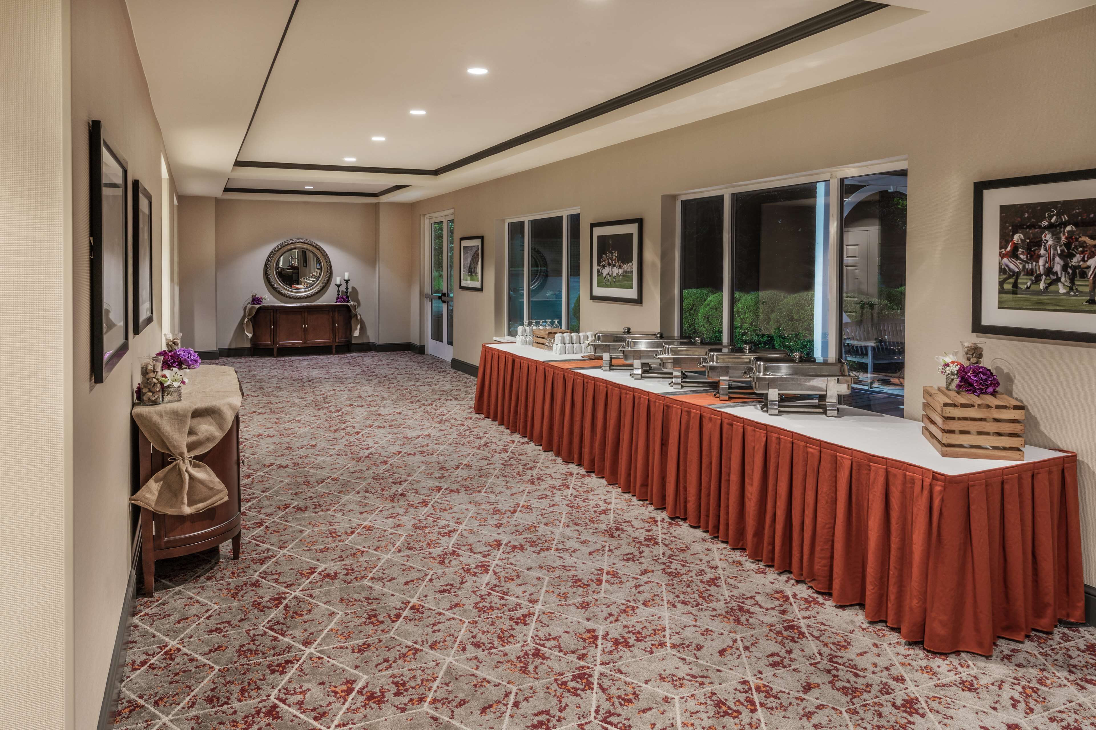 A conference room with a long table covered in a red tablecloth, framed pictures on the walls, and a carpeted floor.