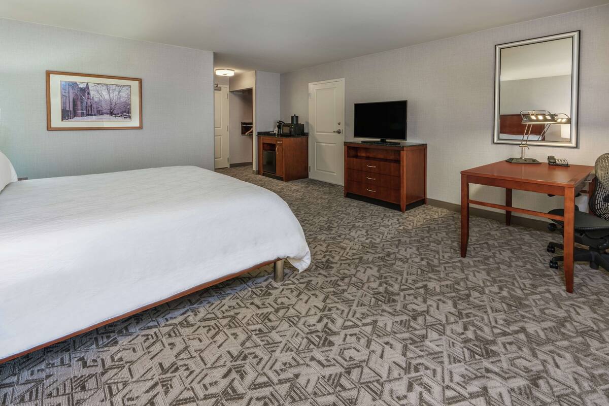 A hotel room with a large bed, a desk with a flat-screen TV, a mirror, and a framed picture on the wall.