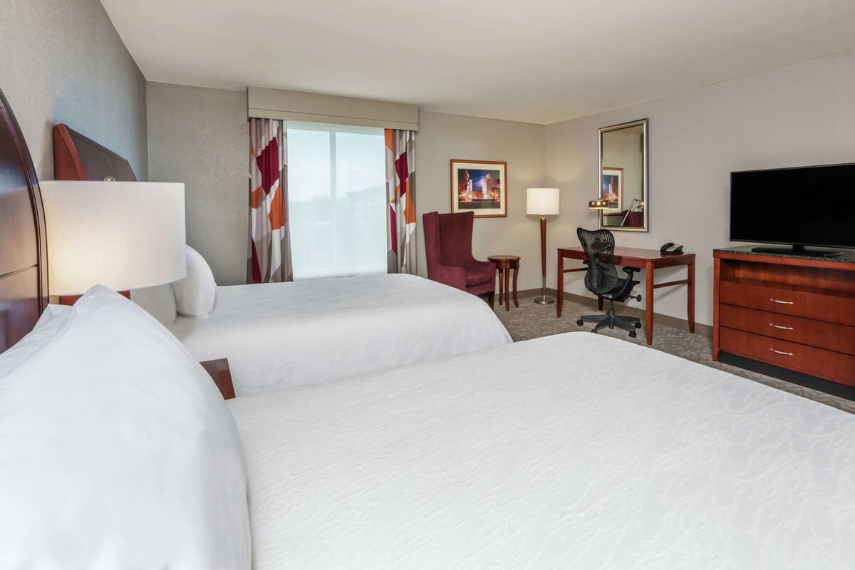 A hotel room with two beds, a desk, a chair, a television, and a dresser.