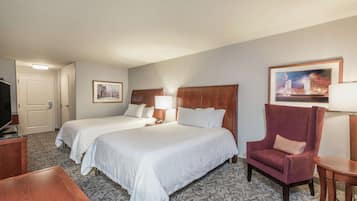 A hotel room with two beds, a wooden armchair, a small table, and a TV.