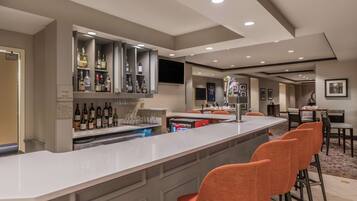 A modern bar area with a long counter, multiple liquor bottles, and orange bar stools.