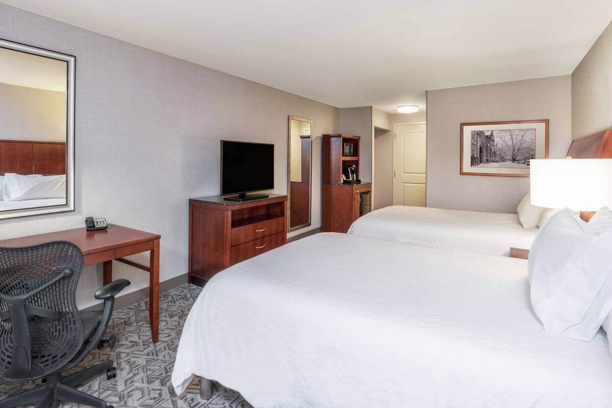 A hotel room with two beds, a desk with a chair, a television, a wardrobe, and a framed picture on the wall.