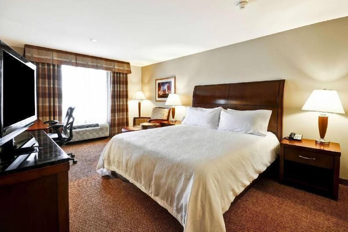 A hotel room with a large bed, two bedside tables with lamps, a flat-screen TV, a desk with a computer, and a window with curtains.