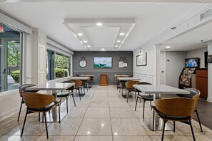 A modern dining area with tables and chairs, a large window, and a wall-mounted TV.