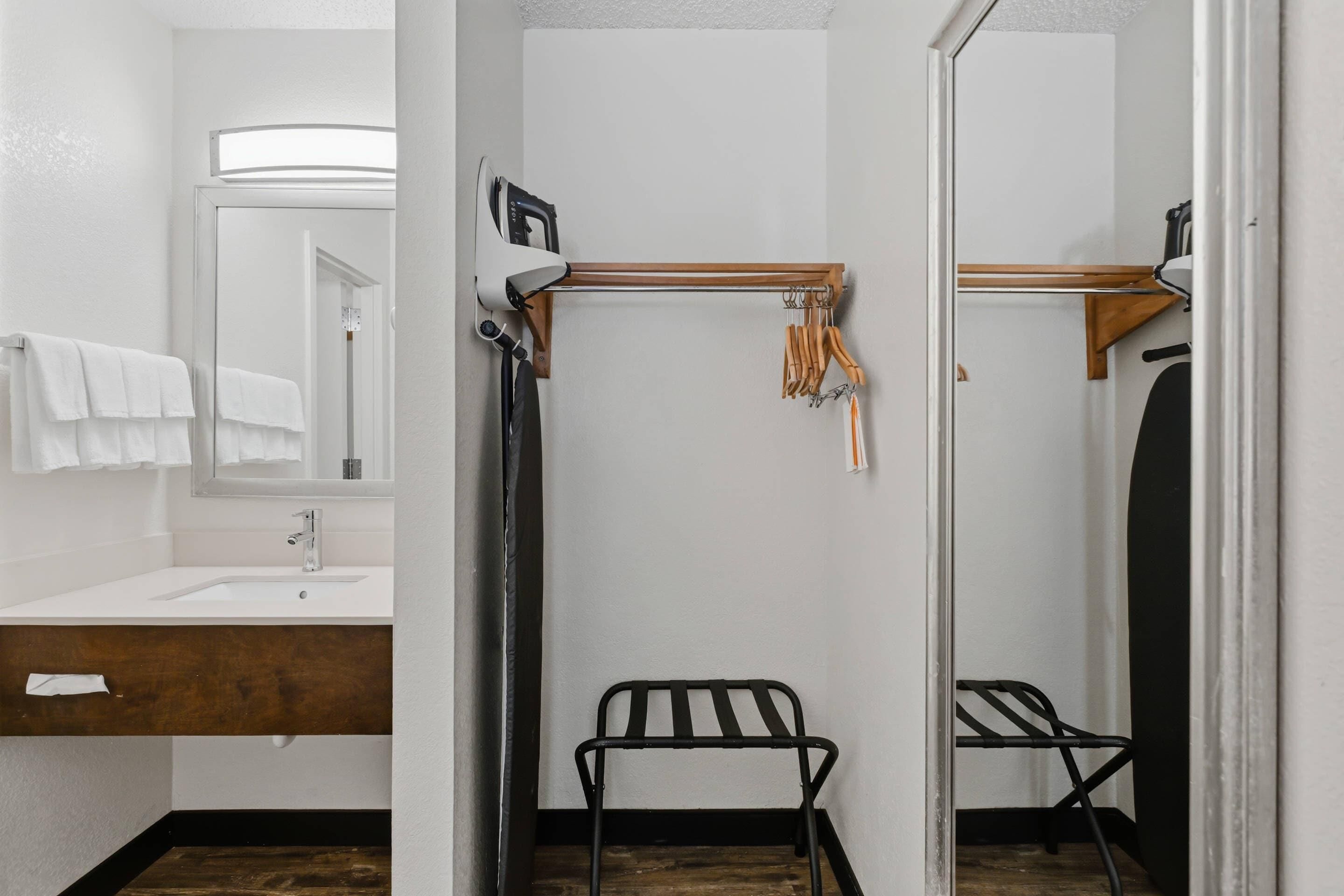 A bathroom with a wooden vanity, a mirror, a towel rack, a shower chair, and a towel rack with towels.
