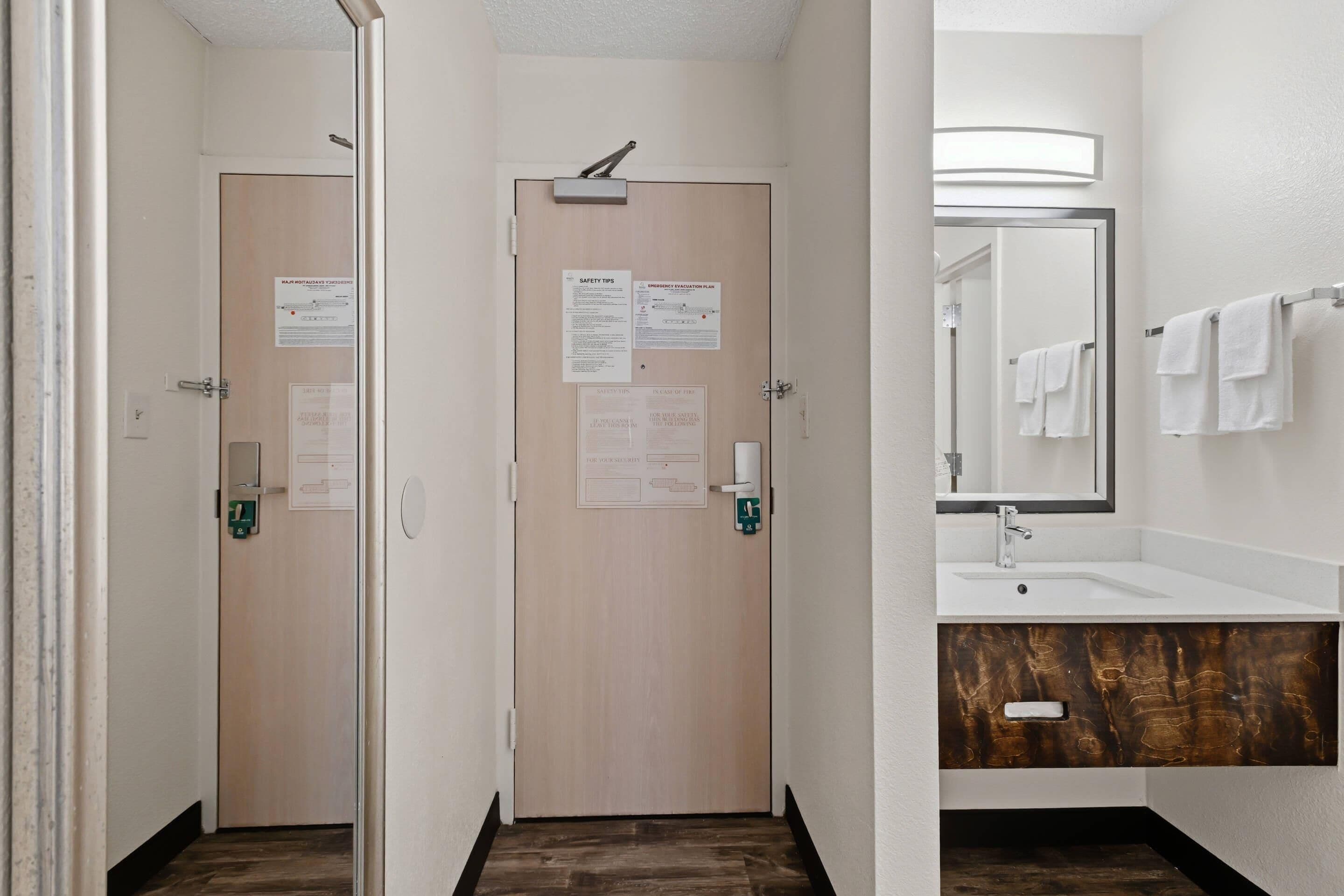 Baño de hotel con tocador de madera, un espejo y dos puertas con información de seguridad y emergencia.