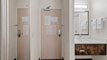 Baño de hotel con tocador de madera, un espejo y dos puertas con información de seguridad y emergencia.
