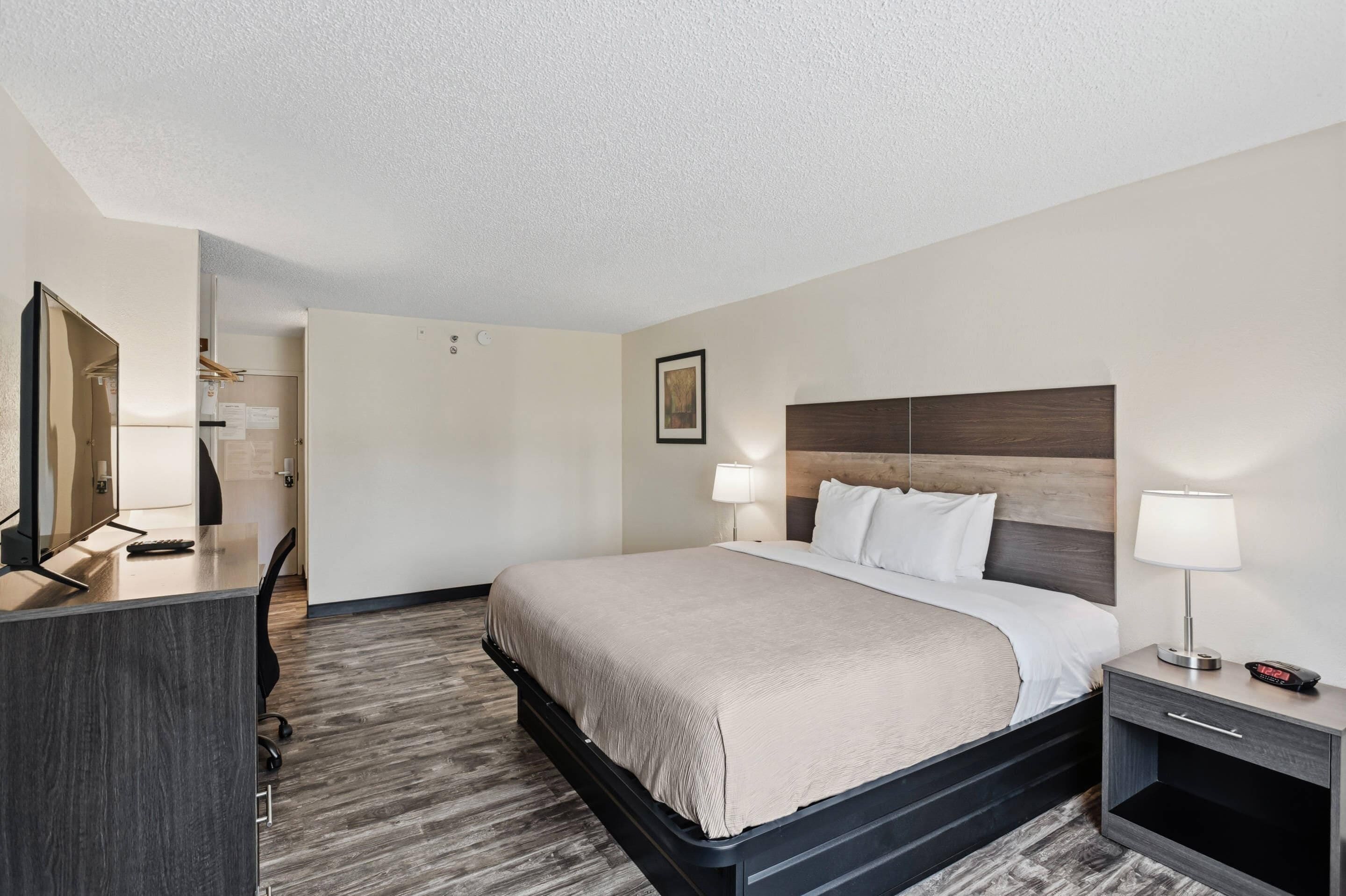 A hotel room with a bed, bedside tables, a desk, and a mirror.