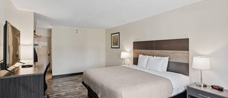 Una habitación de hotel con cama, mesitas de noche, escritorio y espejo.