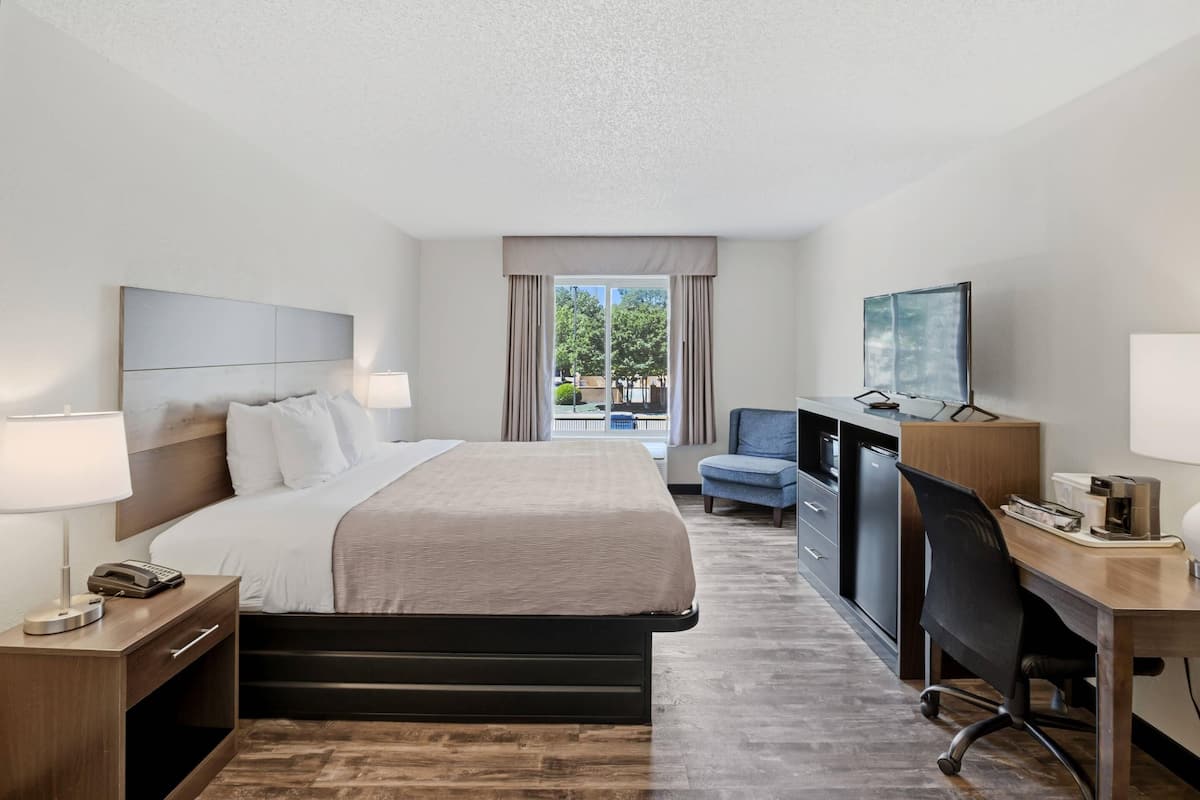 Quarto de hotel com cama, escrivaninha, cadeira, televisão e janela com cortinas.