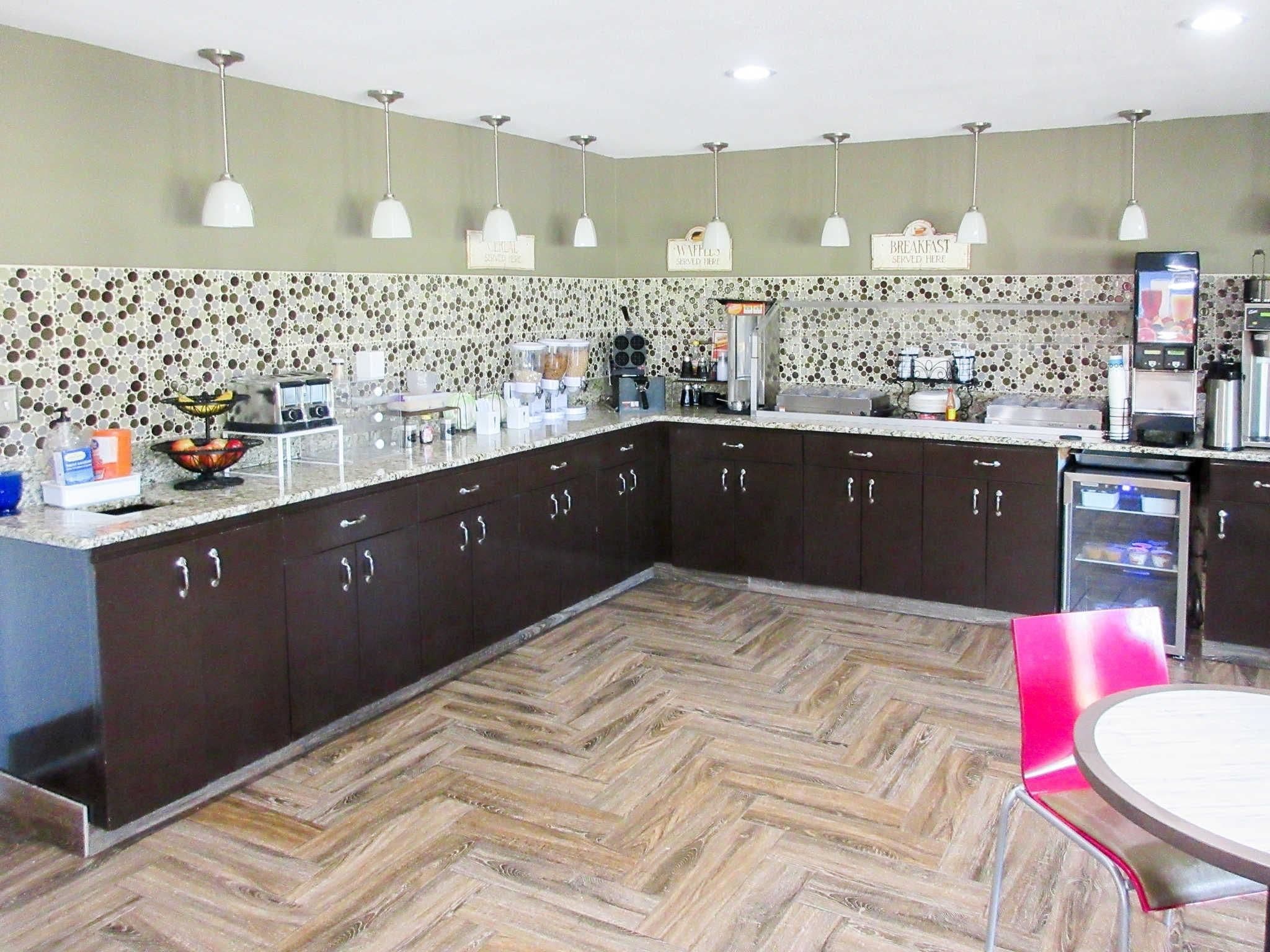 A modern kitchen with dark cabinets, a herringbone wood floor, and a breakfast bar area.
