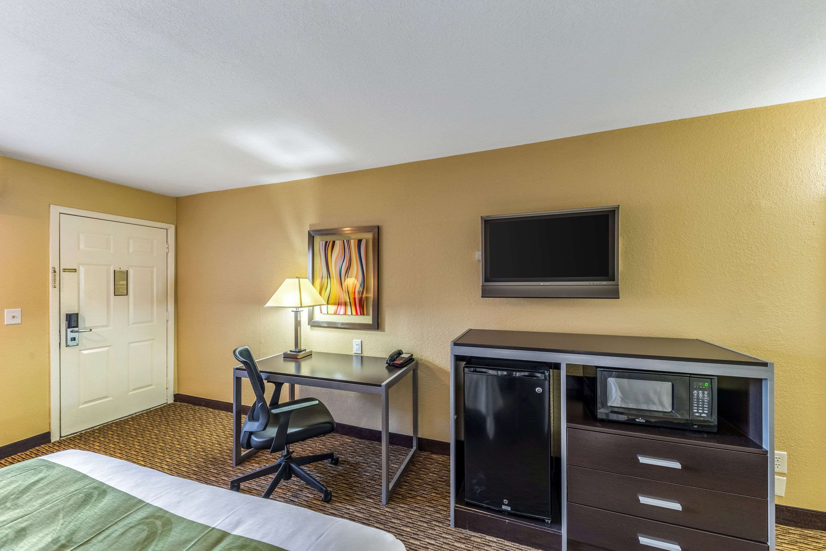 Een hotelkamer met een bed, bureau, stoel, bureaulamp, magnetron en televisie.