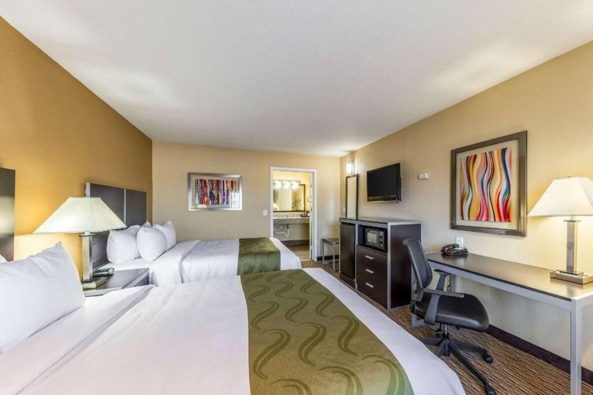 A hotel room with two beds, a desk, a chair, a TV, and a mirror.