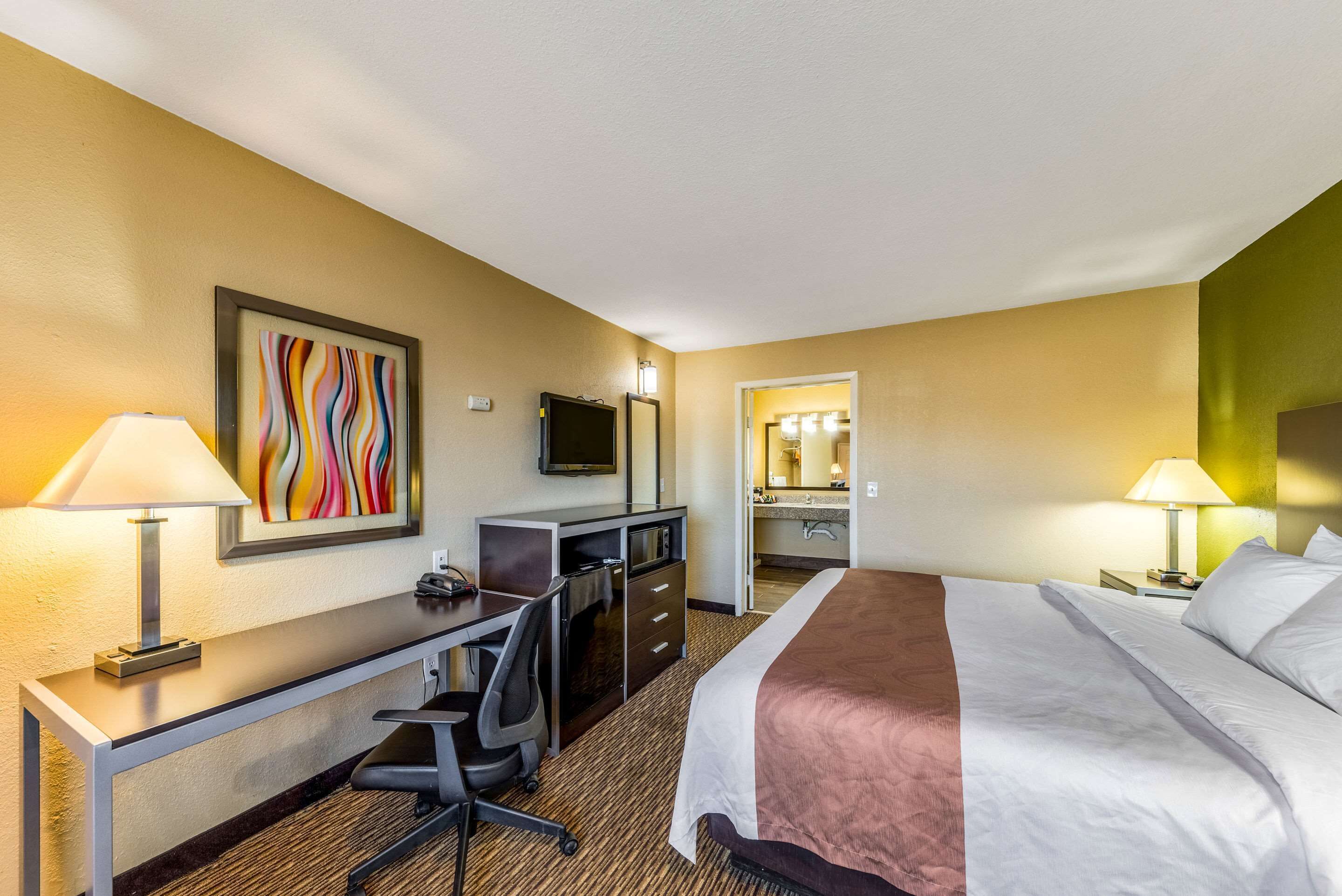 A hotel room with a bed, desk, chair, TV, and a bathroom visible through an open door.