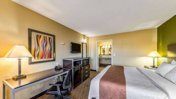 A hotel room with a bed, desk, chair, TV, and a bathroom visible through an open door.