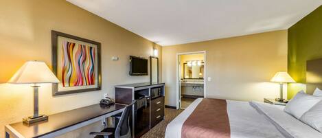 A hotel room with a bed, desk, chair, TV, and a bathroom visible through an open door.