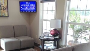 A living room with a sofa, a coffee table with a globe, a lamp, and a TV displaying 'The Admiral Grill'. - Quality Inn Glenpool - Tulsa (Glenpool)