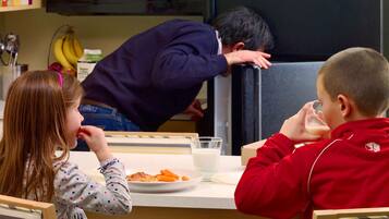 Children dine in a cozy space with a table set for two, surrounded by a kitchen area with a microwave and refrigerator.