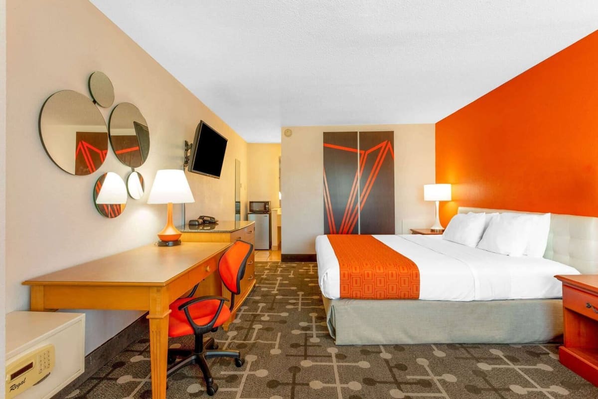 A hotel room with a bed, desk, chair, TV, and two wall-mounted mirrors.