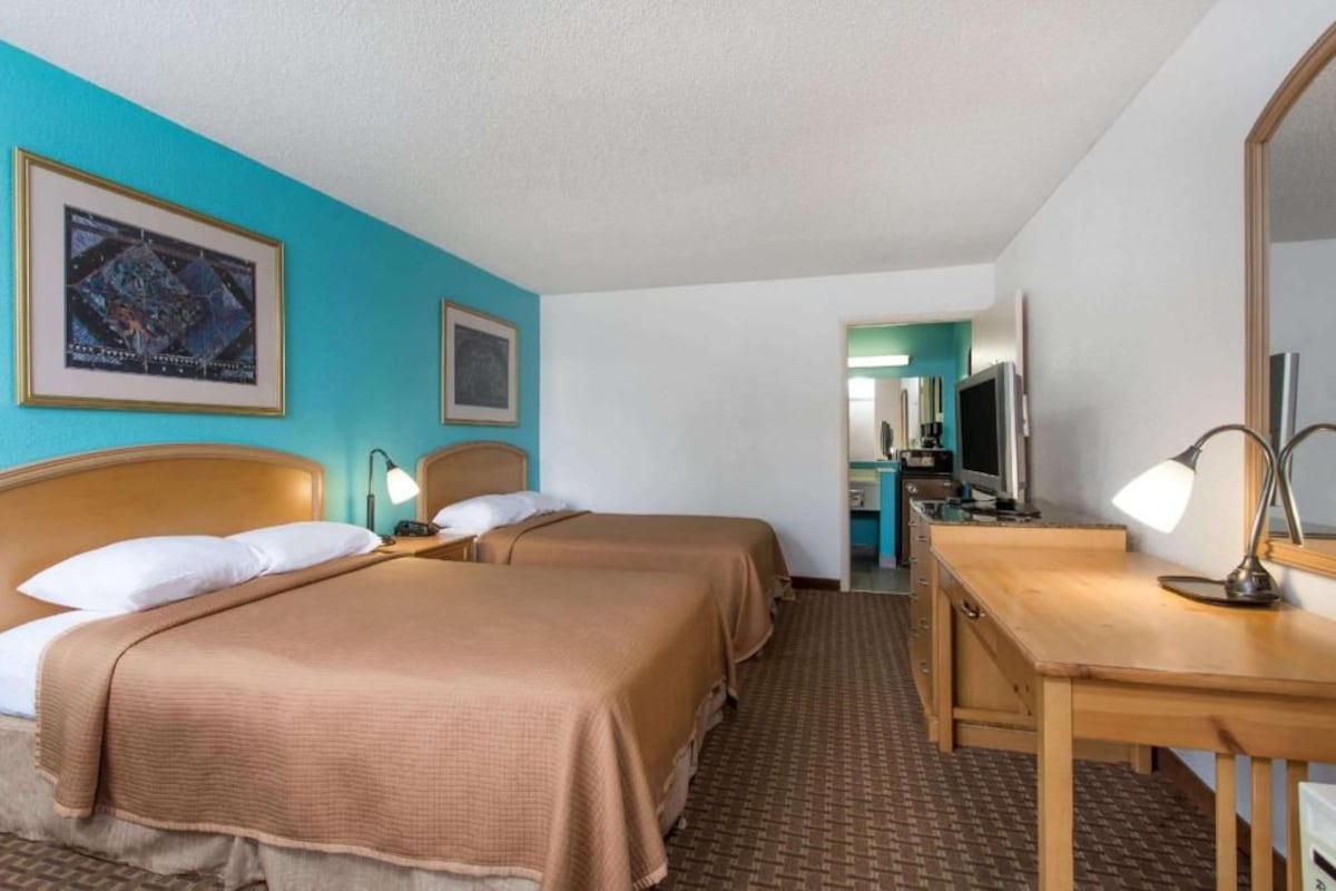 A hotel room with two beds, a desk, a mirror, and a kitchenette.