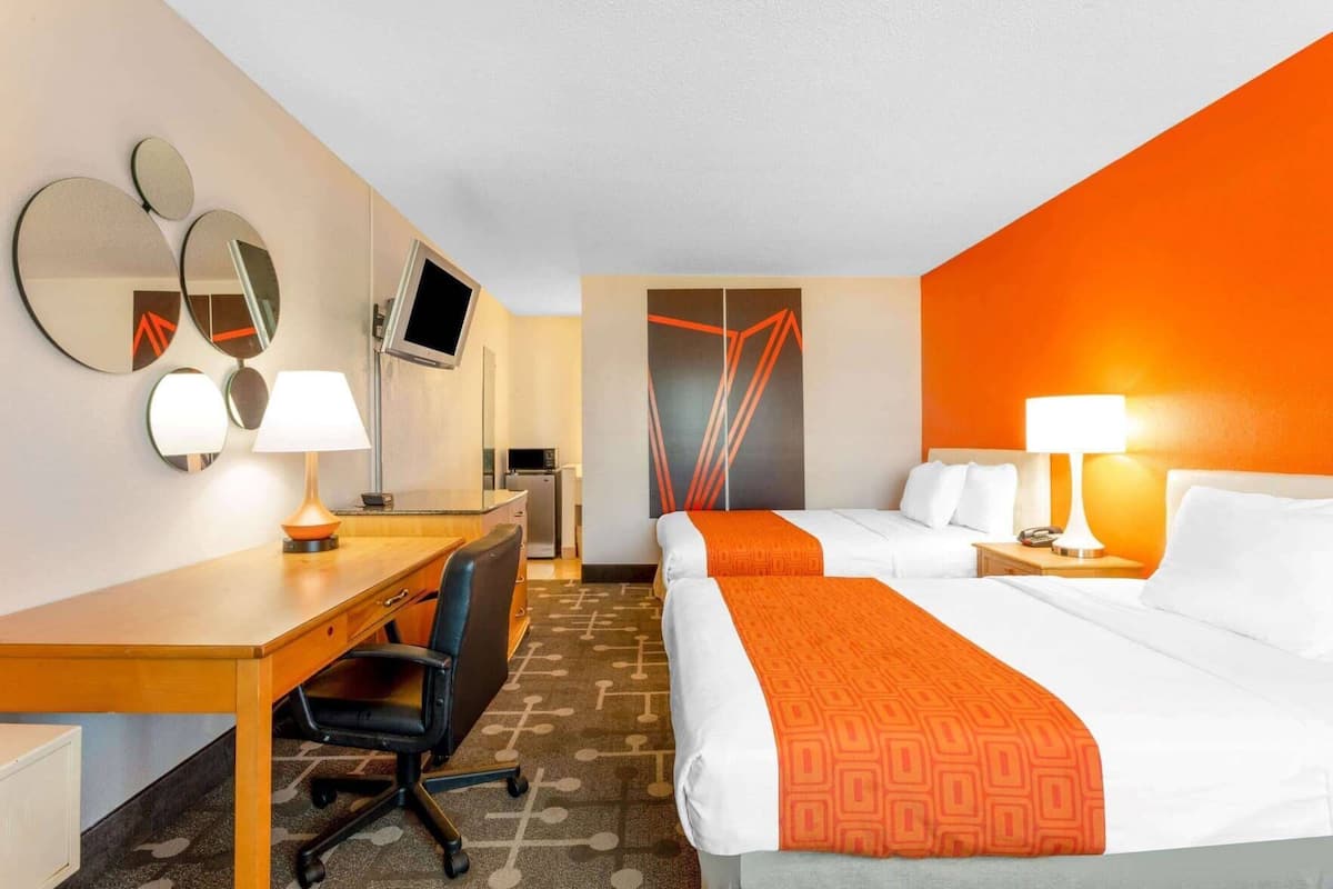 A hotel room with two beds, a desk, a chair, a TV, and a microwave.
