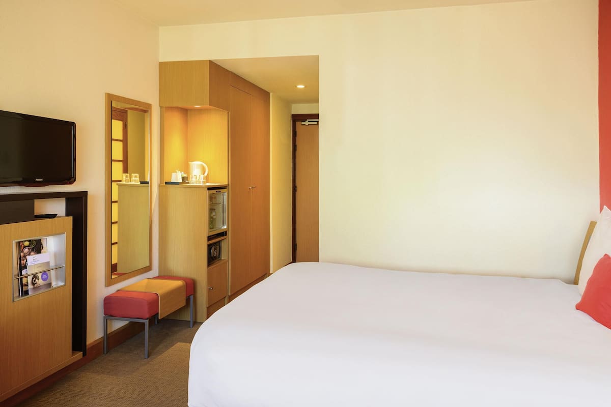 Una habitación de hotel con cama, televisión, escritorio con espejo y una pequeña zona de estar.