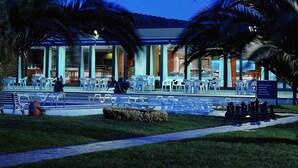 An outdoor seating area with tables and chairs, palm trees, and a building with large windows. - Novotel Porto Gaia (Vila Nova de Gaia)