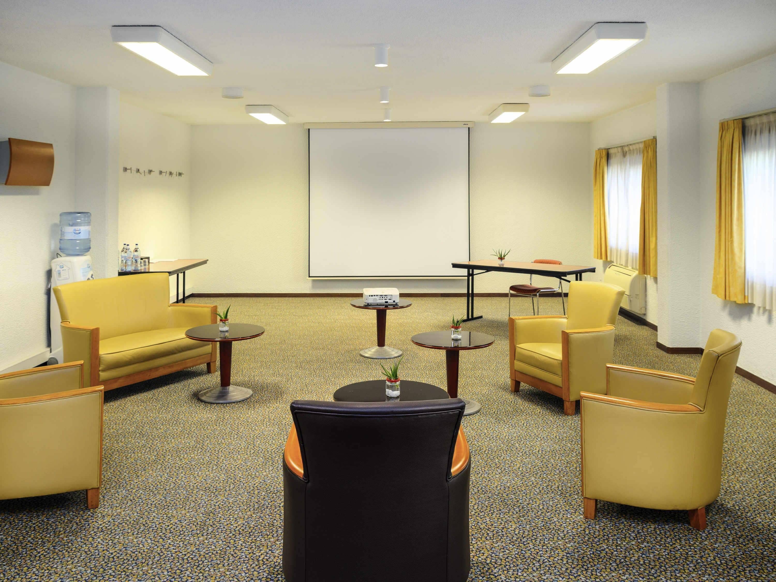 A conference room with a projector screen, a water dispenser, and seating arrangements.