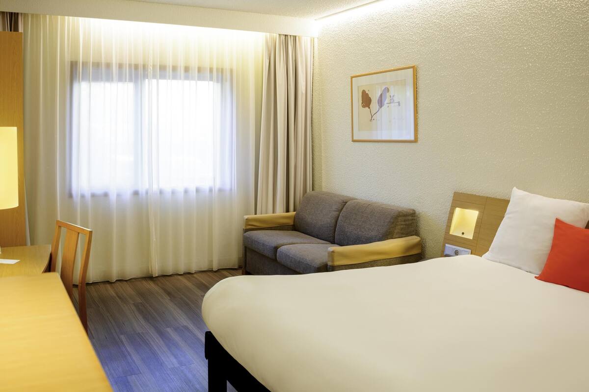 Una habitación de hotel con cama, sofá, escritorio y ventana con cortinas.