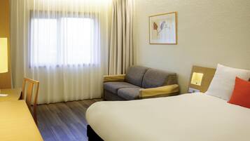 Ein Hotelzimmer mit Bett, Sofa, Schreibtisch und einem Fenster mit Vorhängen.