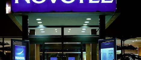 A Novotel hotel entrance with illuminated signage, glass doors, and digital displays.
