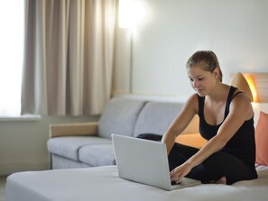 A person using a laptop on a bed in a room with a sofa and a lamp. - Novotel Porto Gaia (Vila Nova de Gaia)
