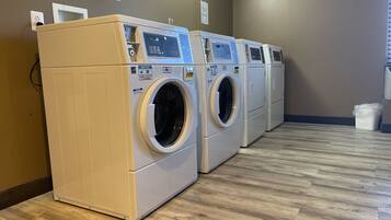 A row of front-loading washing machines in a laundry room with wooden flooring and a brown wall.