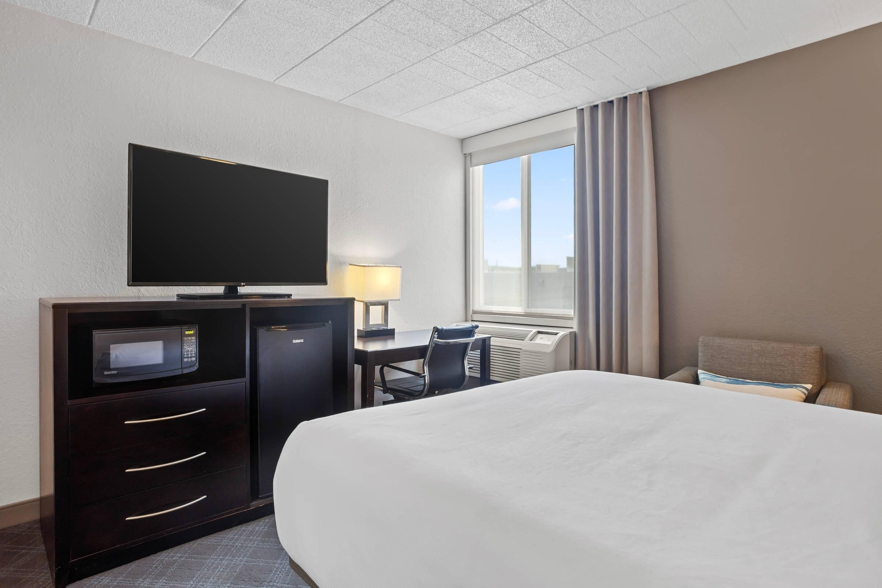 A hotel room with a bed, a desk with a computer, a television, and a window with curtains.