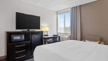 A hotel room with a bed, a desk with a computer, a television, and a window with curtains.