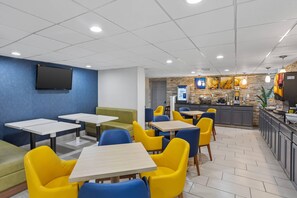 A modern cafe with seating arrangements, a kitchen area, and a flat-screen TV mounted on the wall.