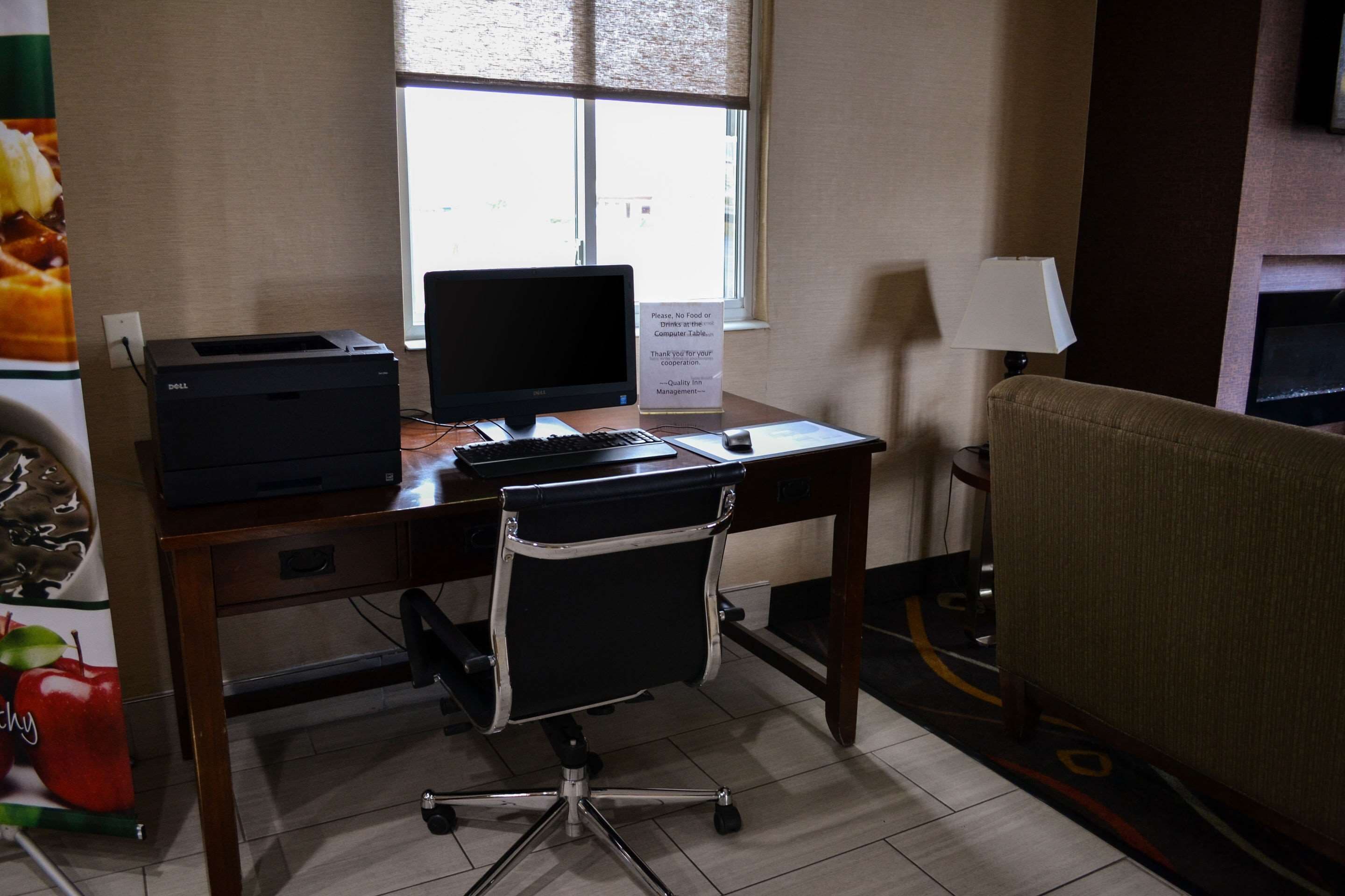 Una habitación de hotel con escritorio, computadora, silla, lámpara y ventana.