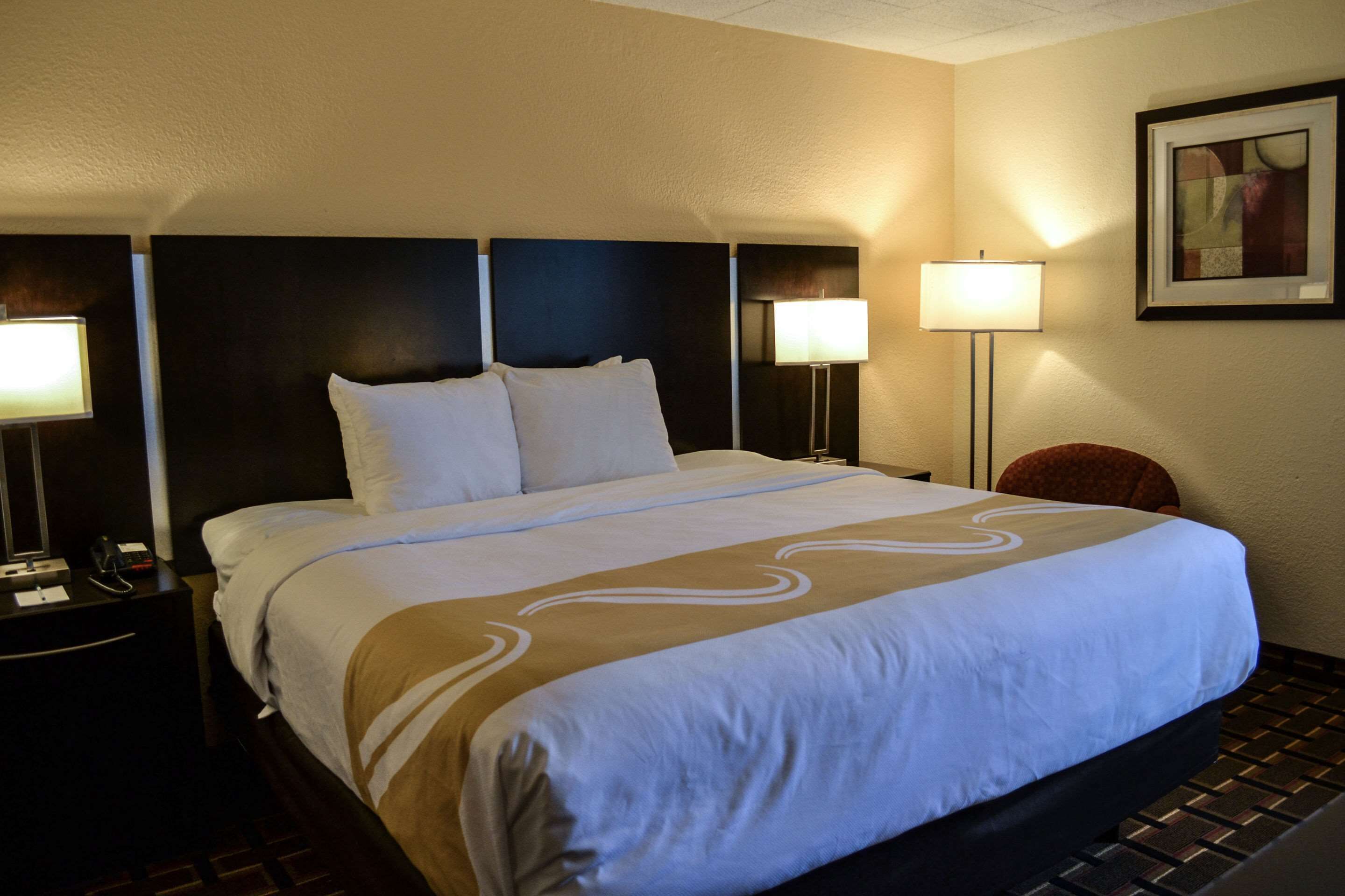 A hotel room with a large bed, two bedside lamps, a nightstand, and a framed picture on the wall.