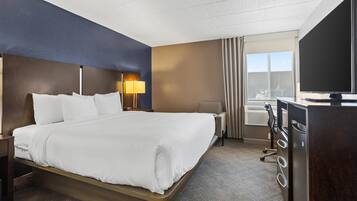 A hotel room with a bed, a desk, a television, and a window with curtains.