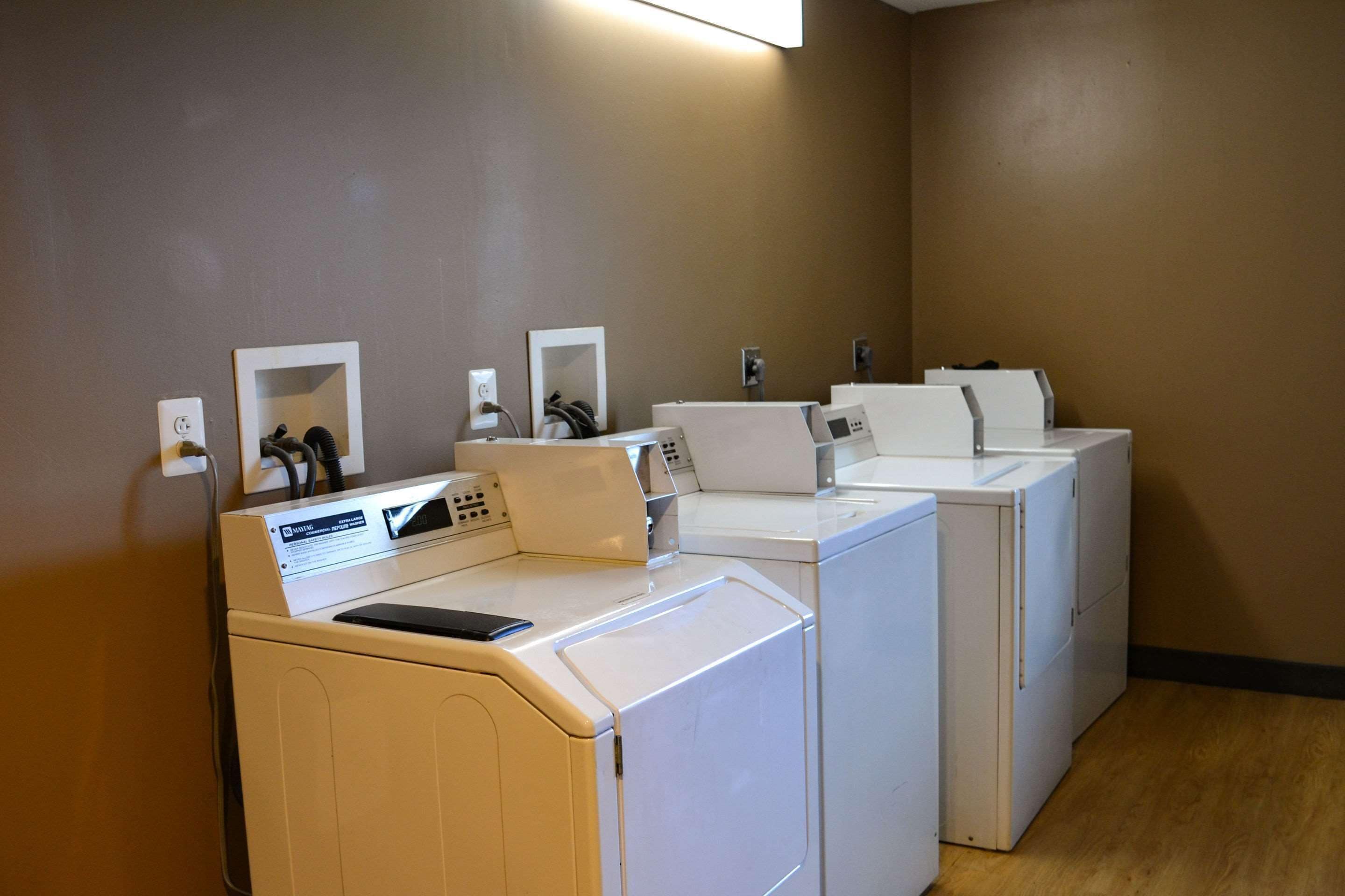 A laundry area with multiple washing machines and dryers, a control panel, and a mirror.