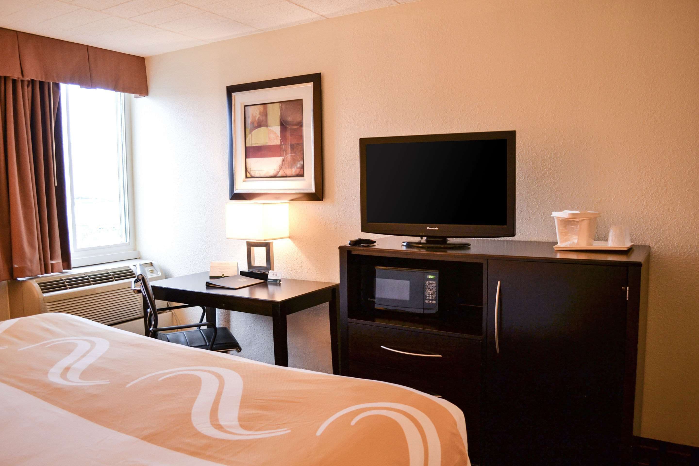 A hotel room with a bed, a desk with a television, a microwave, and a coffee maker.