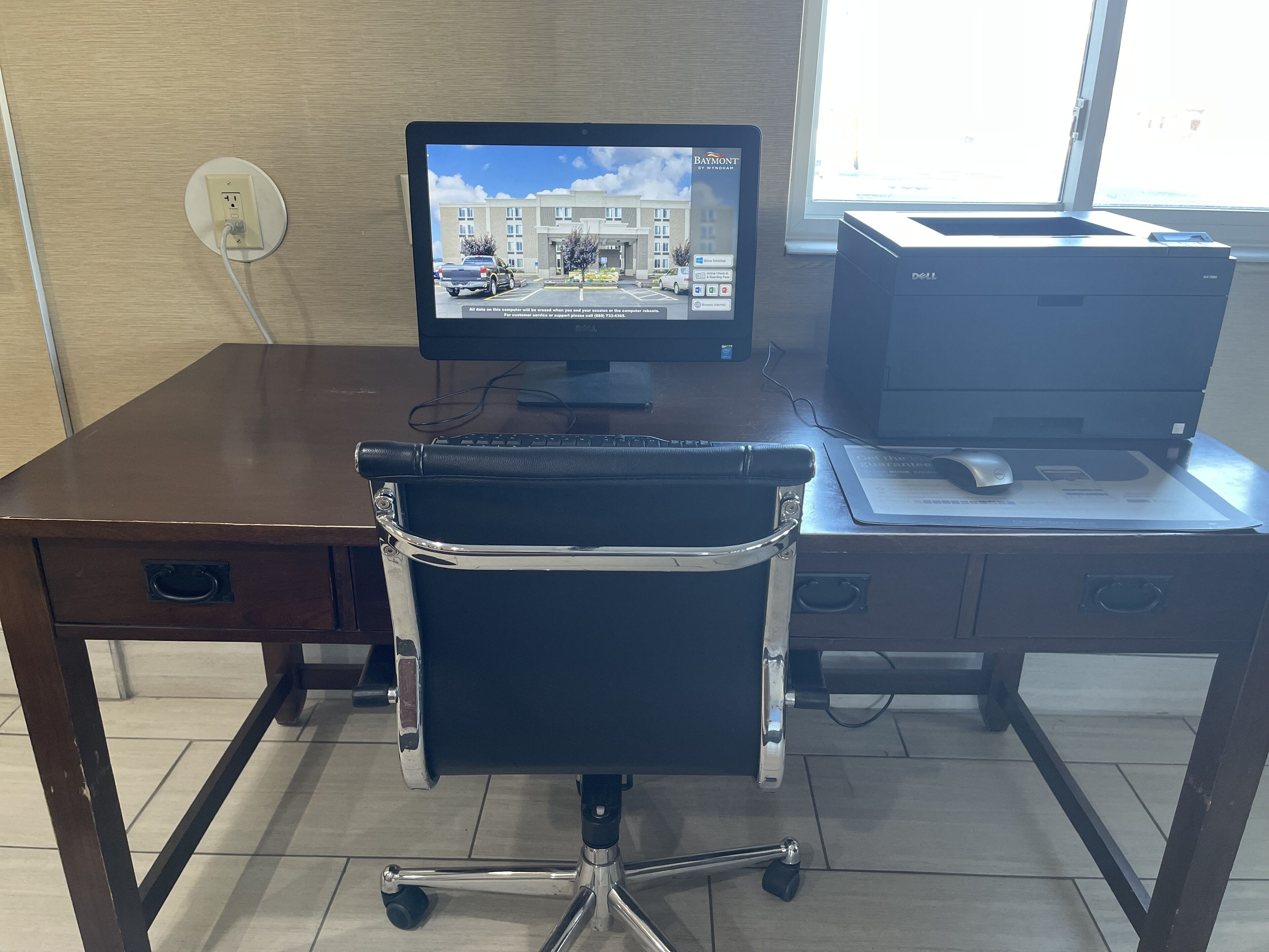 Un escritorio con monitor de computadora, teclado e impresora. Hay una silla frente al escritorio.