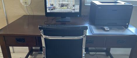 Un escritorio con monitor de computadora, teclado e impresora. Hay una silla frente al escritorio.