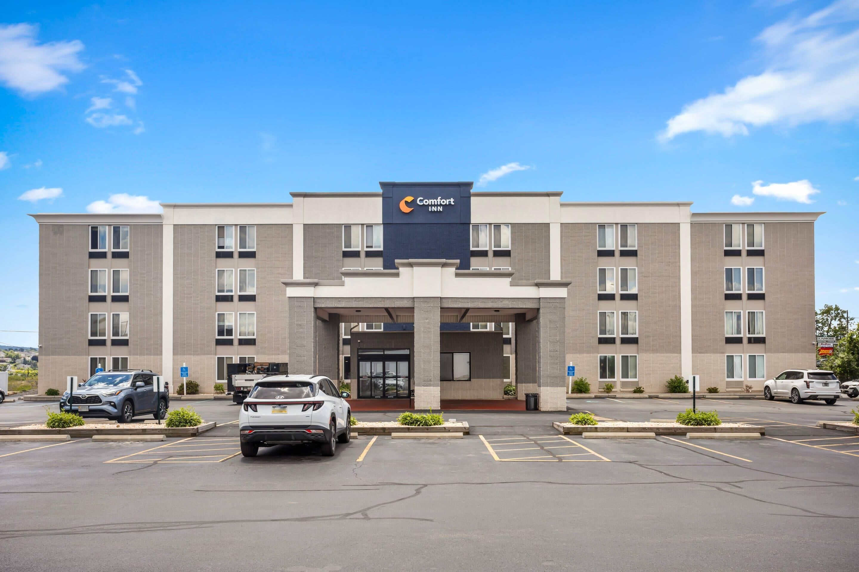 A Comfort Inn hotel with a modern facade, a parking lot, and a clear blue sky.