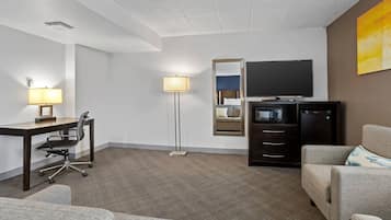 Habitación de hotel con escritorio, silla de oficina, sofá, lámpara de pie, televisor y minibar.